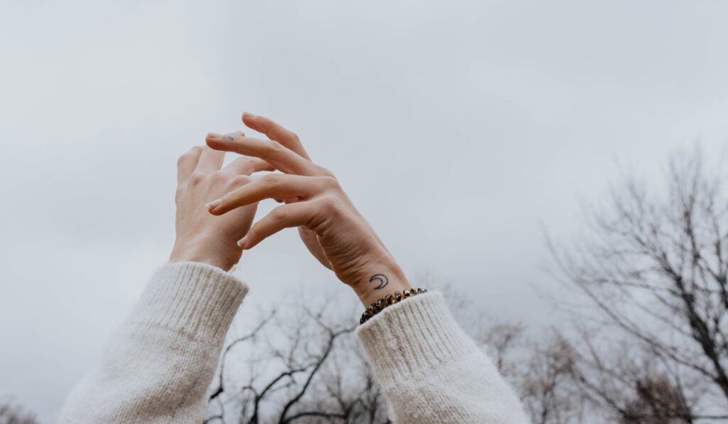 Woman holding her hands in the sky, moon tattoo on wrist.