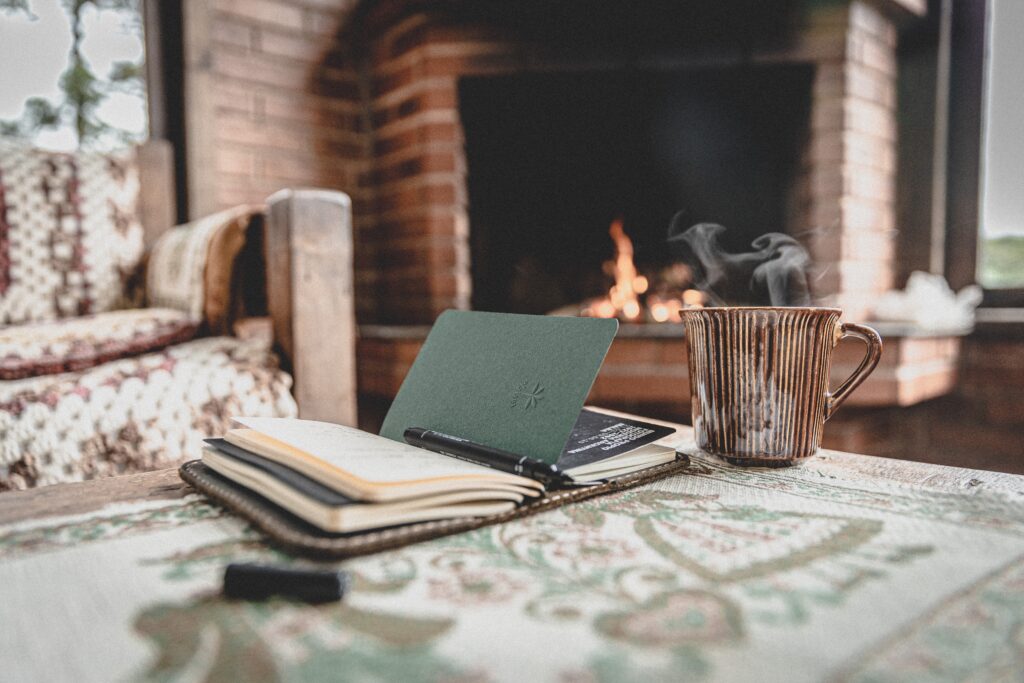 Money attraction journal on a table, in the background the fireplace is burning and a cup of hot cacao is on the table