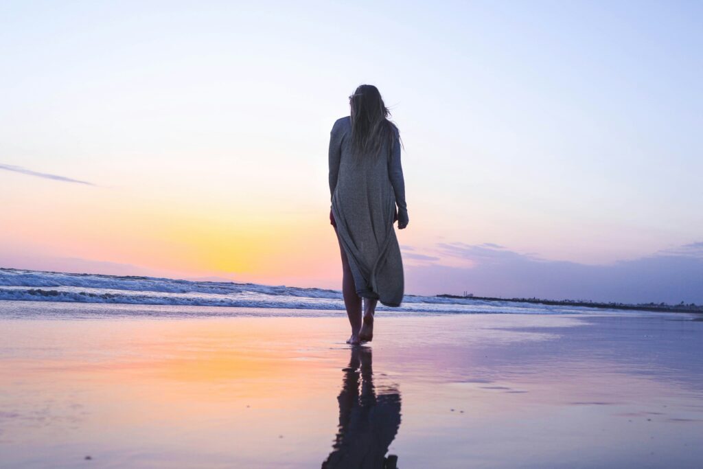 Woman walking on the beach with her feet in the water while the sun is going under