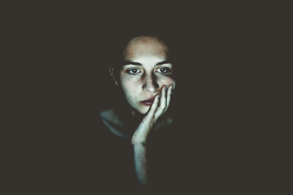 Woman sitting in the dark with her head in her hands looking demotivated